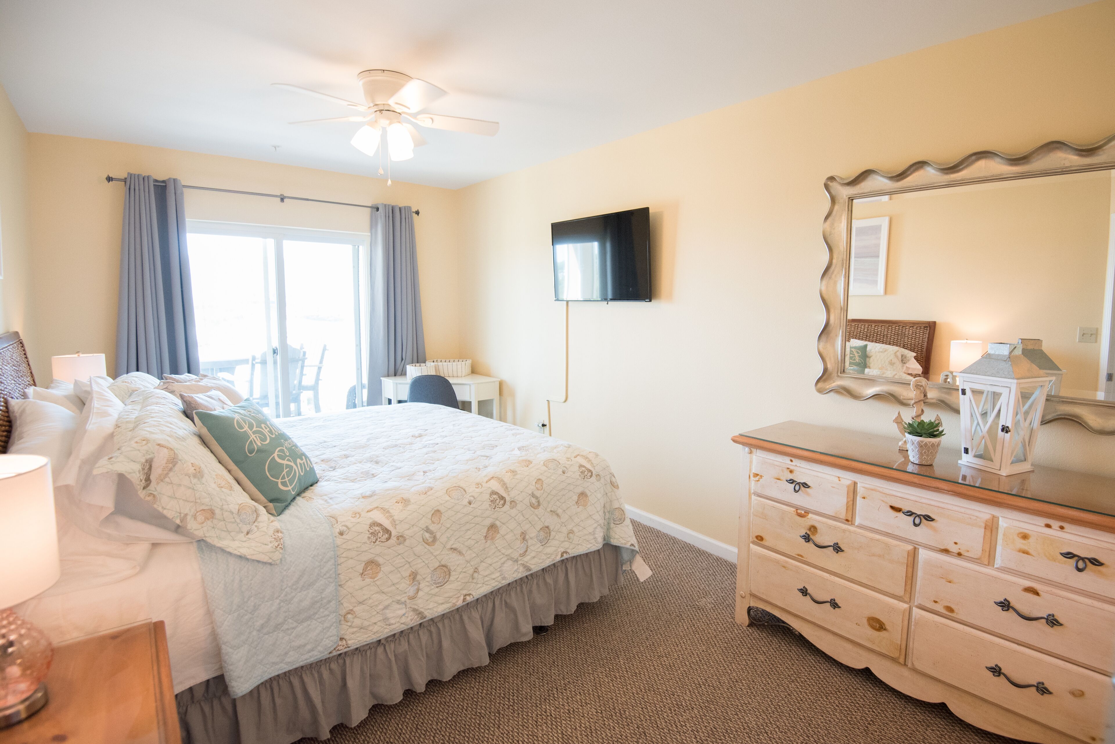 A bedroom with a bed, dresser, mirror, and ceiling fan.