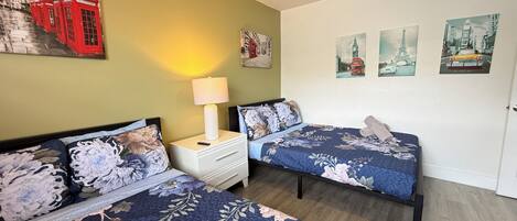 A room with two beds, a nightstand with a lamp, and wall art including a red telephone booth and cityscape pictures.
