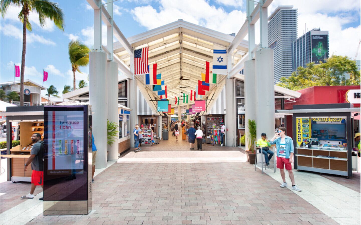 A pedestrian walkway with shops and kiosks, featuring flags and a clear sky.