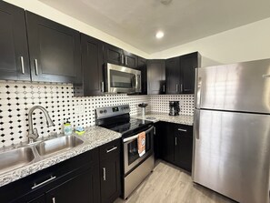 A modern kitchen with black cabinets, stainless steel appliances, and a tiled backsplash.
