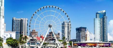 A waterfront cityscape with a large Ferris wheel, modern high-rise buildings, and a Hard Rock Cafe.