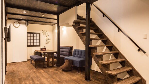 Un intérieur moderne avec un escalier en bois, un coin repas comprenant une table et des chaises, et un espace détente avec un canapé et un pouf.