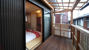 A room with a sliding glass door leading to a balcony. The room has a wooden floor and a bed with red bedding. - Kyomachiya Gion Miyagawatei (Kyoto)