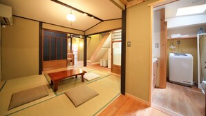 A traditional Japanese room with tatami flooring, a low wooden table, and a sliding door leading to a kitchen area with a refrigerator. - Kyomachiya Gion Miyagawatei (Kyoto)