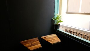 Two wooden stools against a dark wall near a window with a potted plant. - 2Street Hostel at Surathani - Adults Only (Surat Thani)