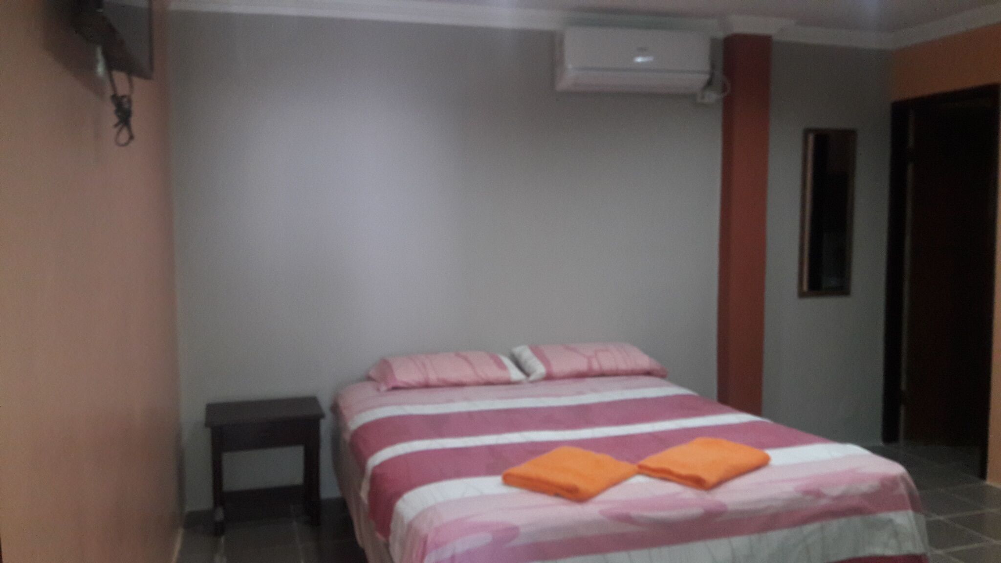 A bedroom with a bed, a nightstand, and an air conditioning unit on the wall.