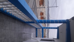A corridor with blue and white walls, a tiled floor, and a view of buildings in the background. - Hotel Brisas del Pacifico (Playas)