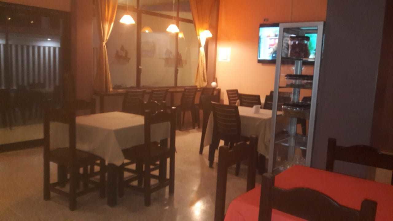 Un comedor con mesas y sillas, una barra con vitrina y una pantalla de televisión.