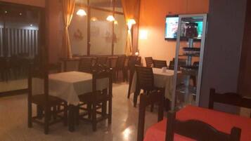Un comedor con mesas y sillas, una barra con vitrina y una pantalla de televisión.
