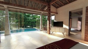 A modern, open-plan bedroom with a large window overlooking a swimming pool and lush greenery. - 7 Chakras Resort (Kerobokan)