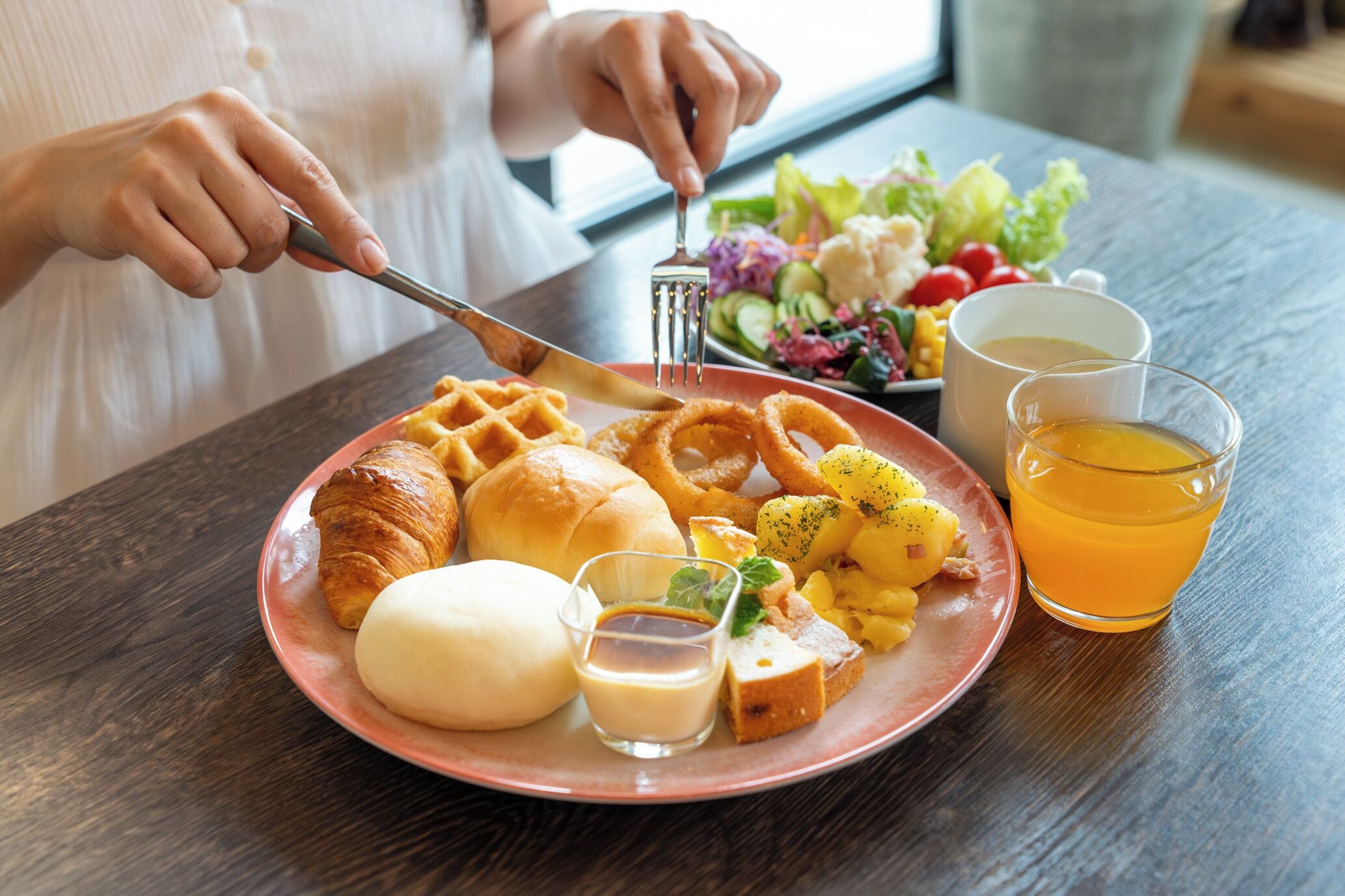 A plate of food including croissants, bread rolls, and potatoes, with a glass of orange juice and a cup of tea.