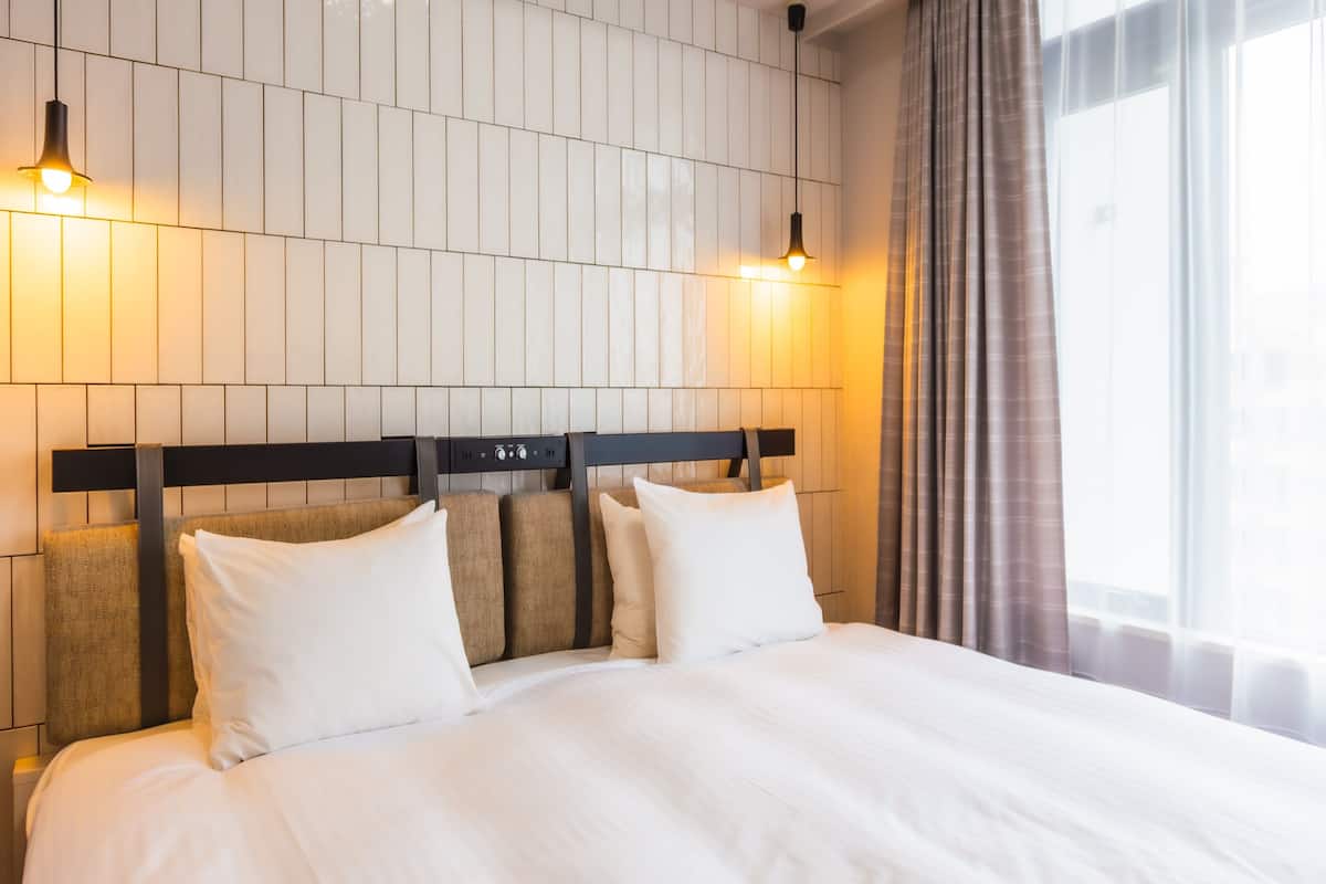 Una cama bien tendida con sábanas blancas, un cabecero de madera y dos lámparas de pared.