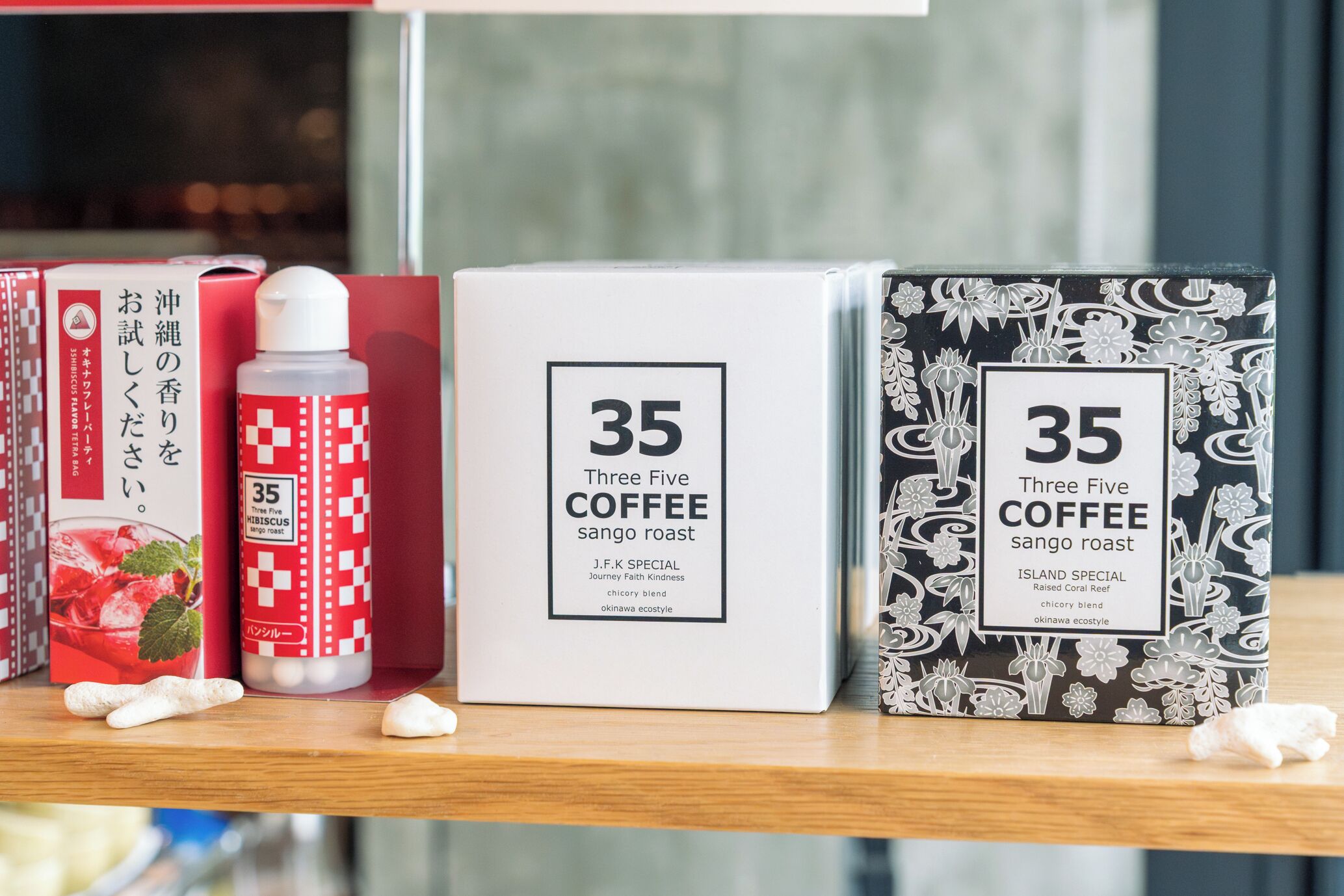 A shelf with three boxes of 'Three Five Coffee' and a bottle of 'J.F.K. Special' on a wooden surface.
