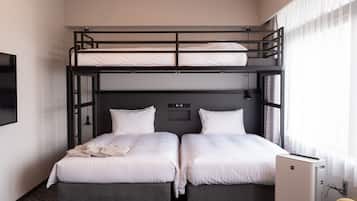 A hotel room with two beds, a bunk bed above, a flat-screen TV, and a small desk with a lamp.