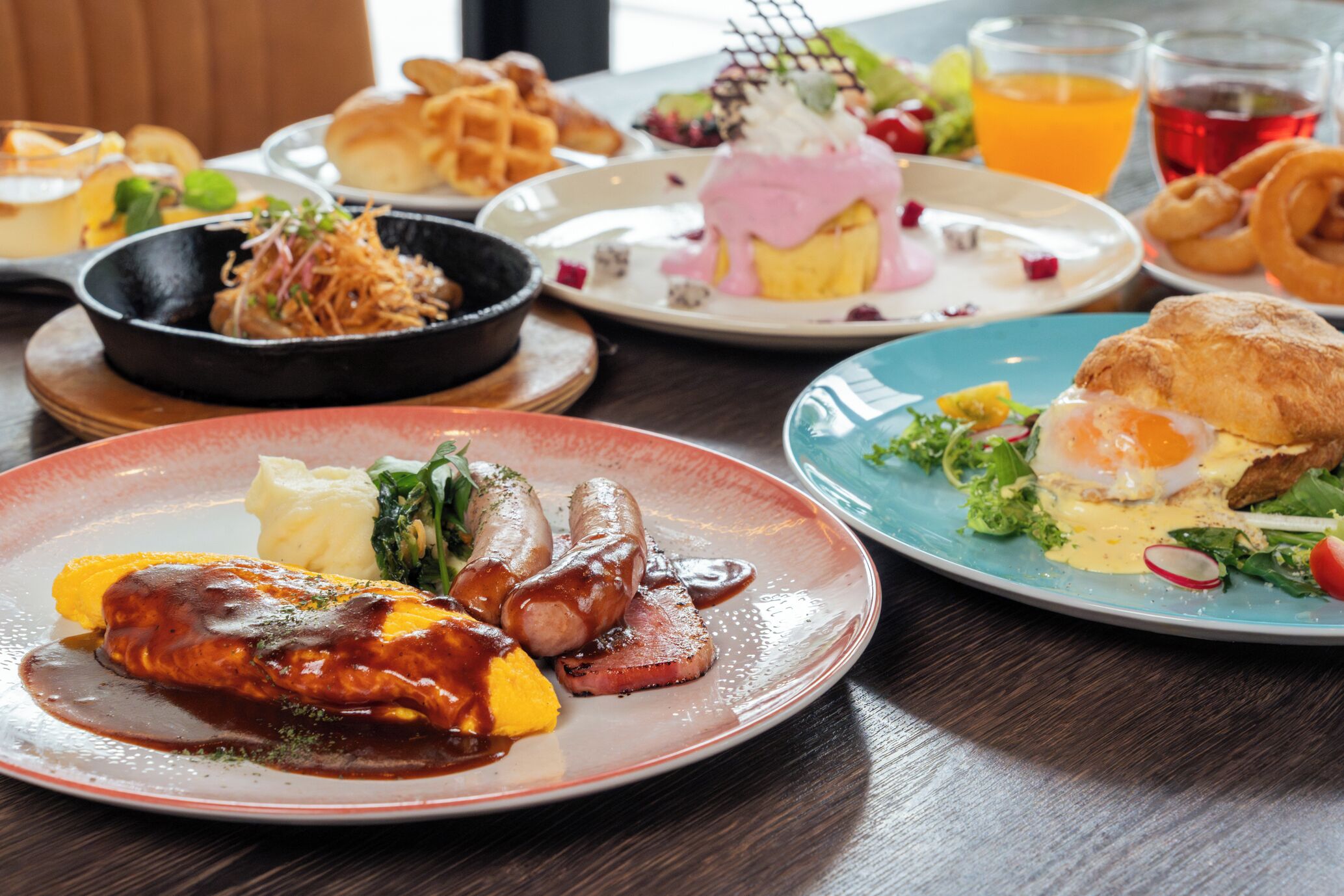 A dining table with various dishes including a steak, sausages, and a plate with a poached egg and vegetables.