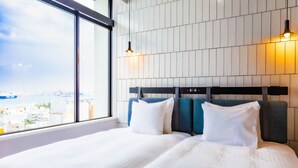 A hotel room with a large window, a bed with white bedding, and a headboard with a control panel. - Hotel Cocktail Stay Naha (Naha)