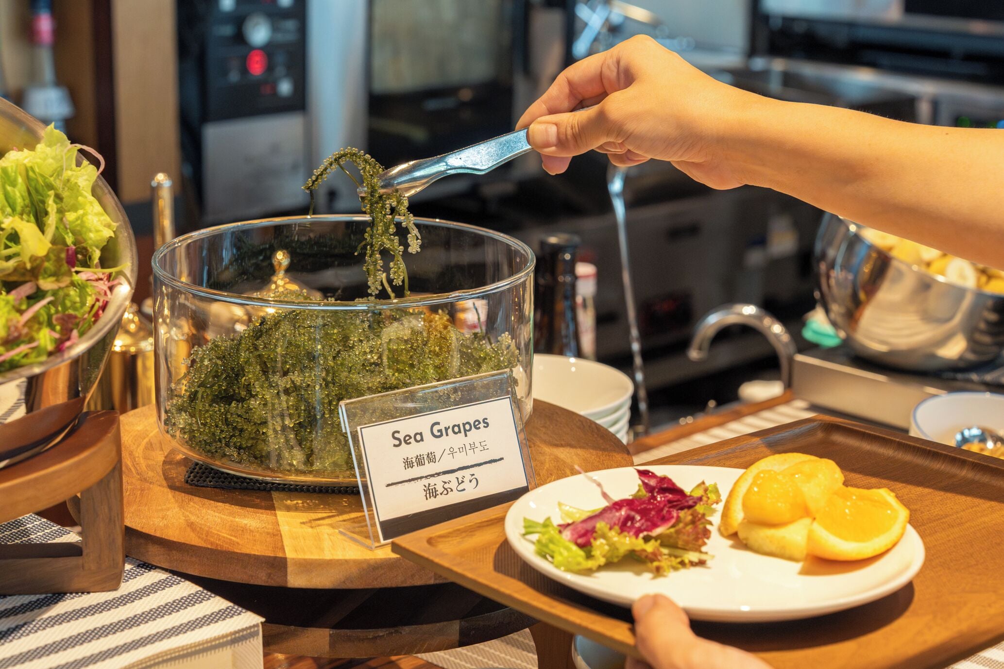 A buffet with a sign for 'Sea Grapes' and a person serving themselves.
