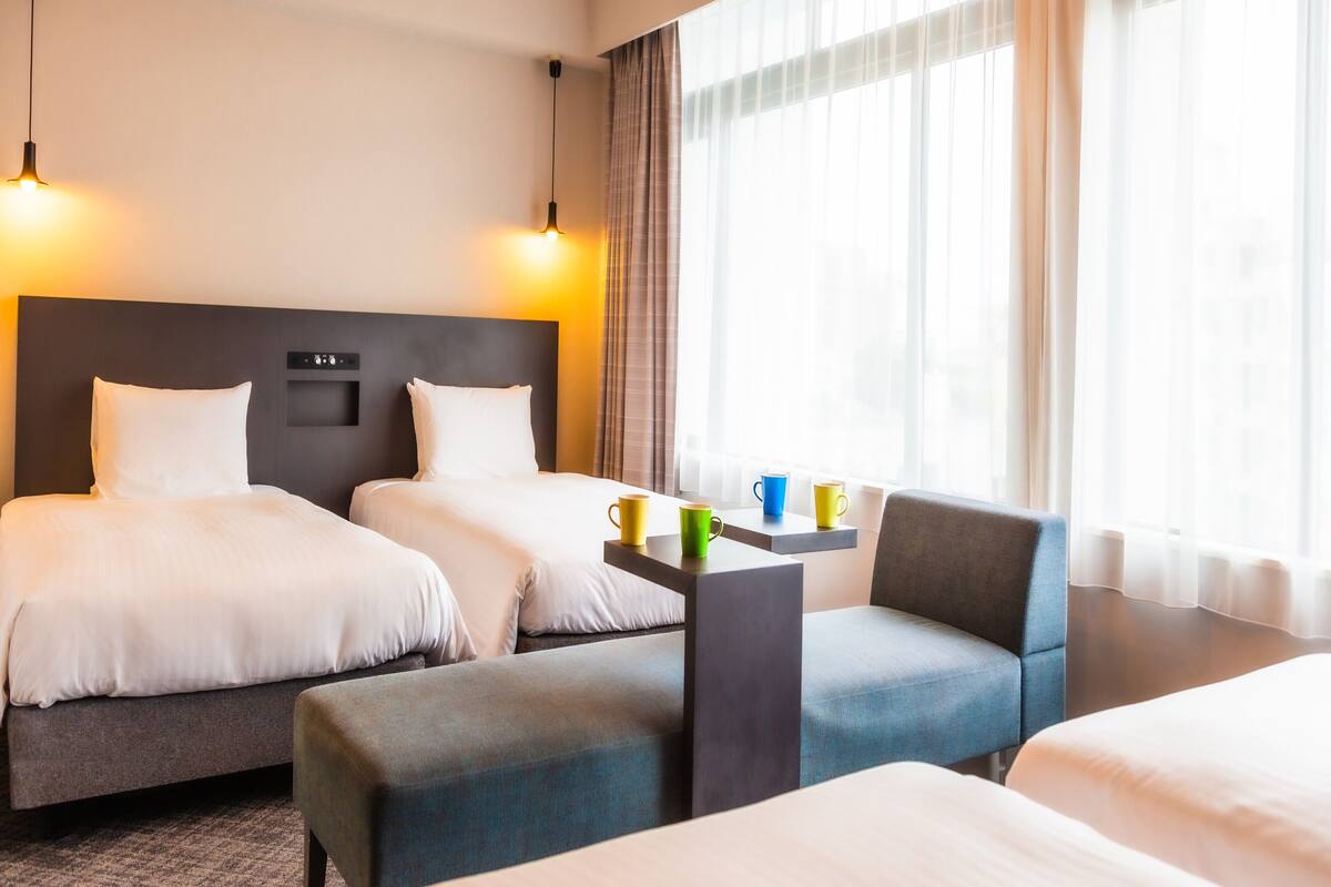 Una habitación de hotel con dos camas, un sofá, una mesita y una ventana con cortinas.