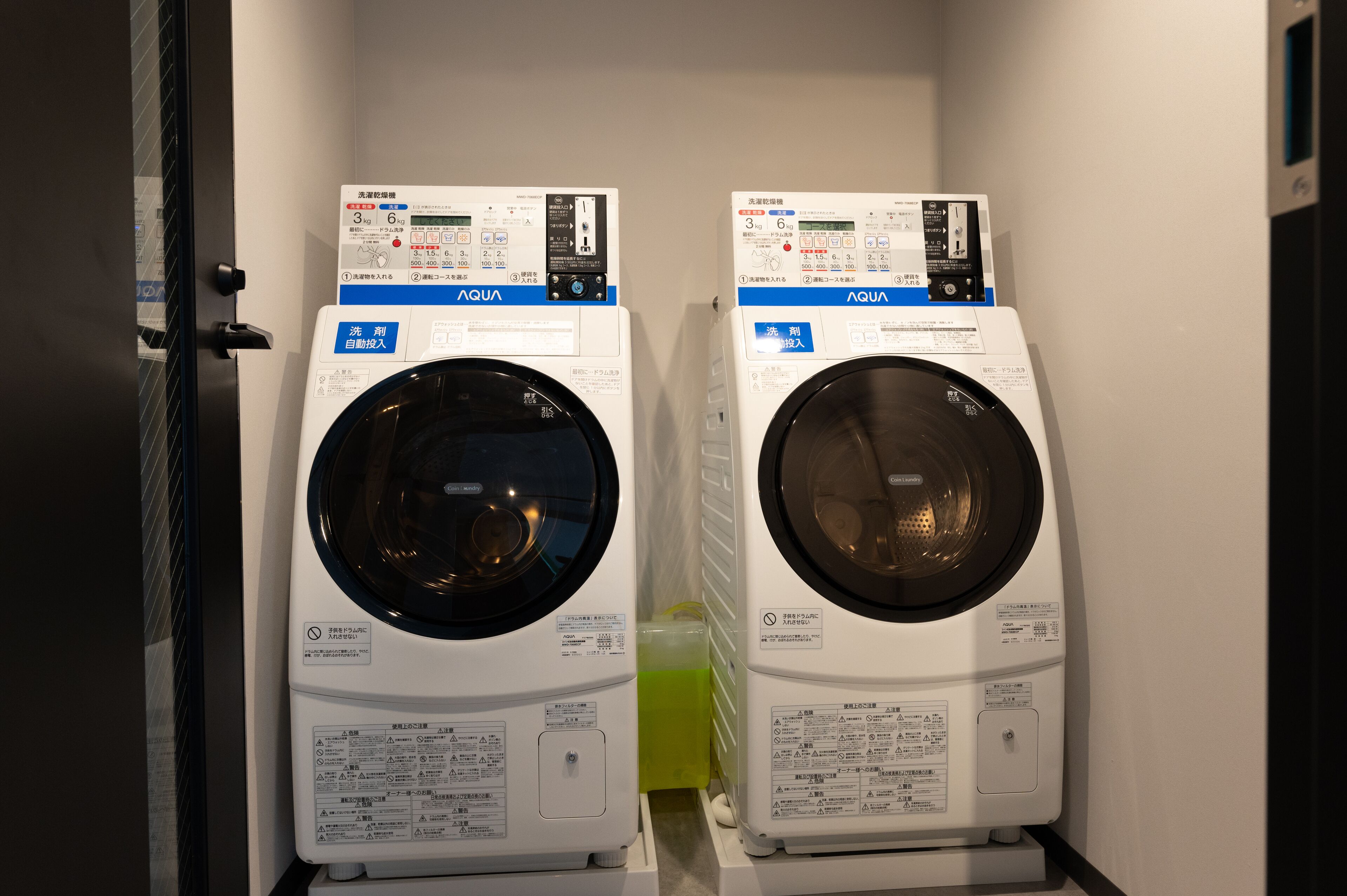 Two front-loading washing machines in a laundry room with control panels and safety instructions.