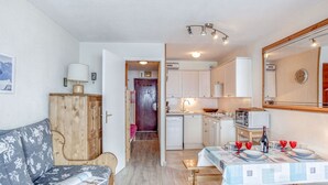 A compact living space with a sofa, a dining table set for four, a kitchen area with cabinets and a microwave, and a hallway leading to a door. - Lovely apartment for 4 people with WIFI, TV and balcony (Les Boisses)