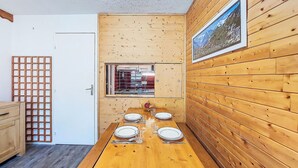 Uma sala de jantar de madeira com uma mesa comprida posta para quatro pessoas, uma janela com vista e uma porta à esquerda.