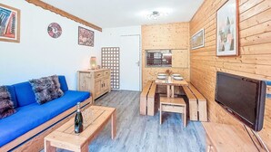 Uma sala de estar acolhedora, com um sofá azul, mesa de centro de madeira e um canto de jantar com mesa e cadeiras de madeira.