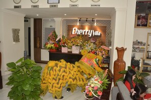 A reception area with a large sign reading "Cherry Villa," a decorative plant, and a traditional lion dance costume. - Cherry Villa (Hue)