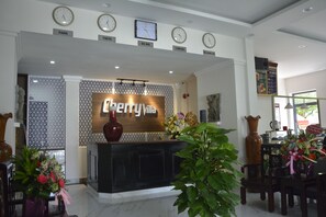 A hotel reception area with a modern design, featuring a reception desk, clocks displaying different city times, and a large floral arrangement. - Cherry Villa (Hue)