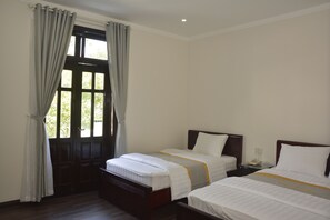 A hotel room with two single beds, a wooden door, and a window with curtains. - Cherry Villa (Hue)