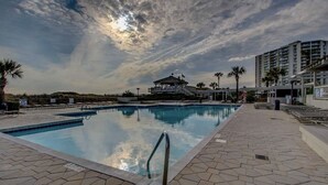 En swimmingpool med et redningstårn, palmer og en moderne bygning i baggrunden.