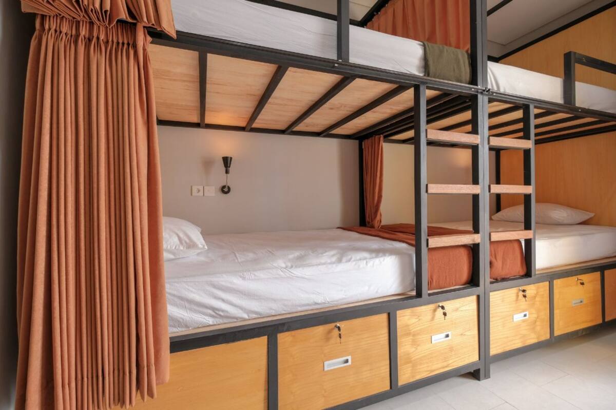Camera con letto a castello, struttura in legno, biancheria bianca e tenda sul lato sinistro.