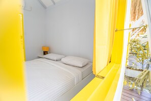 A room with a bed, a nightstand, and a window with a view of plants. - Canggu Castle - Hostel (Canggu)