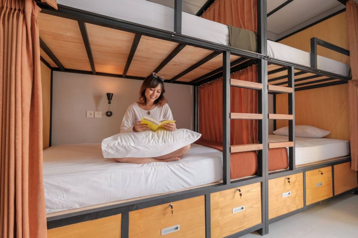 Camera con letto a castello e una persona che legge un libro. Sono presenti cassetti portaoggetti sotto il letto e una lampada fissata alla parete.