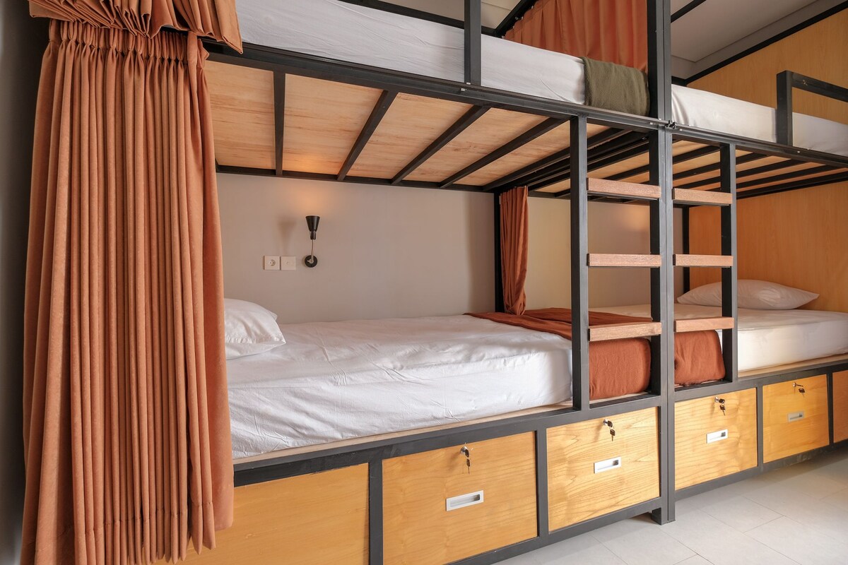 A bunk bed room with a wooden ladder, a white mattress, and a curtain.