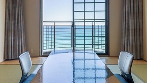 A room with a large table, two chairs, a view of the sea through a window with a metal grid, and traditional tatami mats on the floor. - Hotel Riviera Shishikui (Kaiyo)