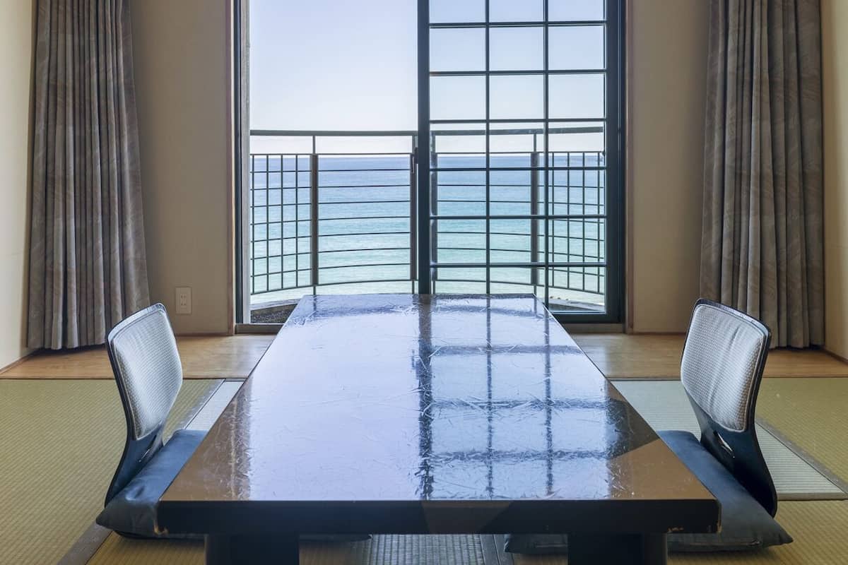 A conference room with a large table, two chairs, and a view of the sea through a window with a metal grid.