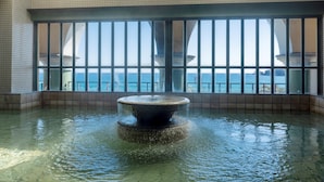 A pool with a central fountain, surrounded by tiled walls and large windows offering a view of the sea. - Hotel Riviera Shishikui (Kaiyo)