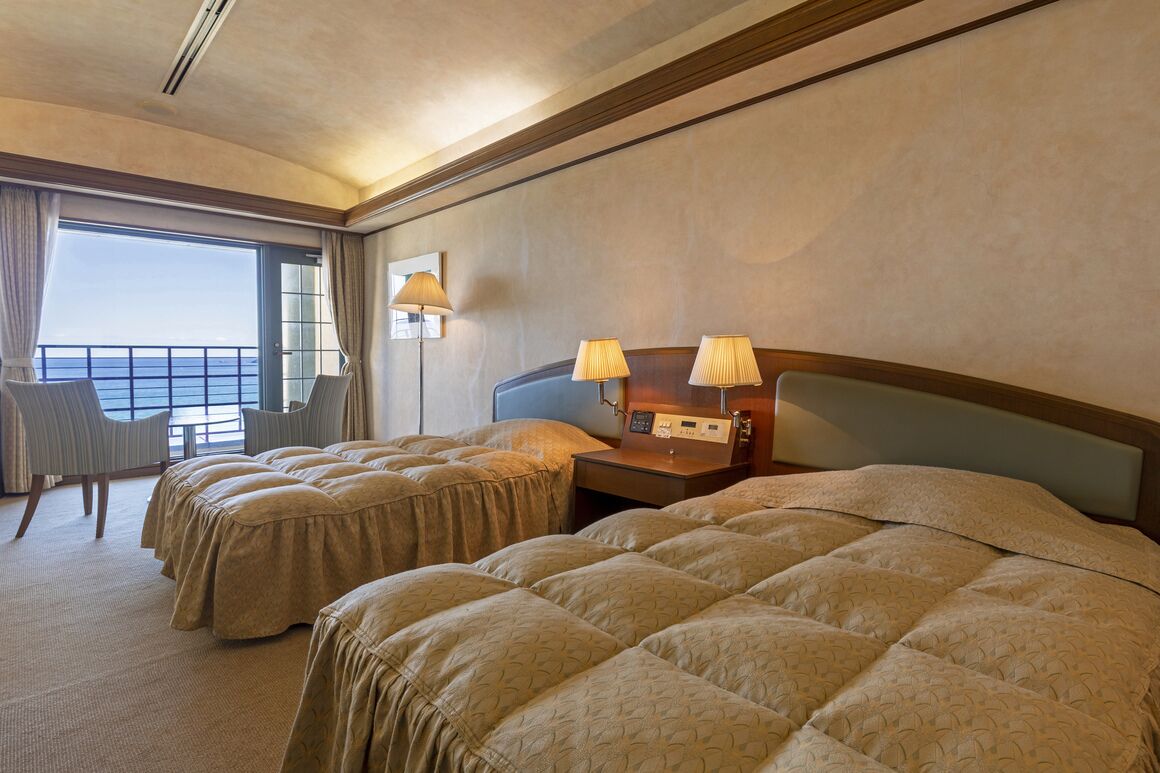 Una habitació d'hotel amb dos llits, un escriptori amb làmpades, una cadira i una finestra gran amb cortines.