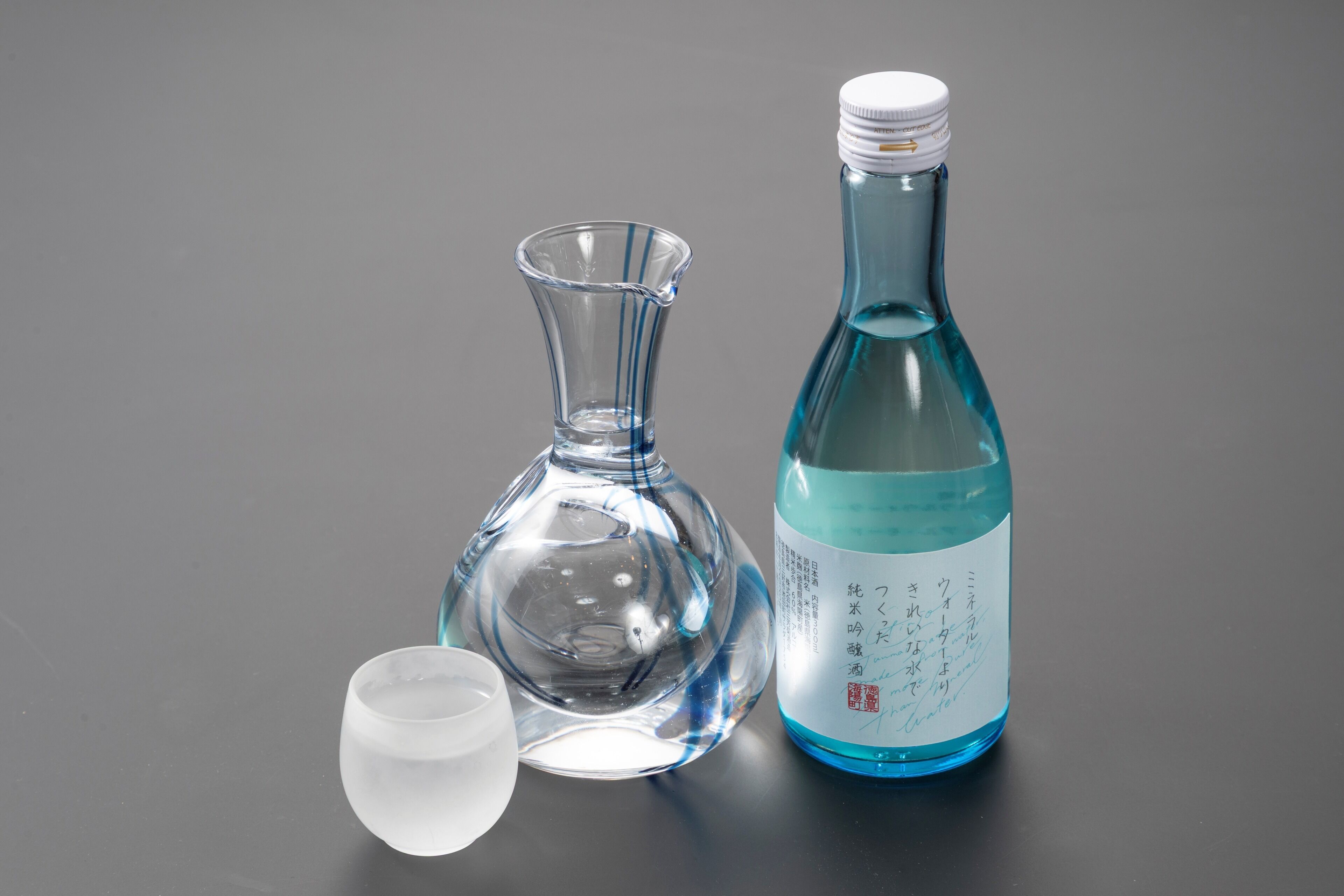 Een heldere glazen fles met een blauw etiket en een heldere glazen karaf op een tafel.