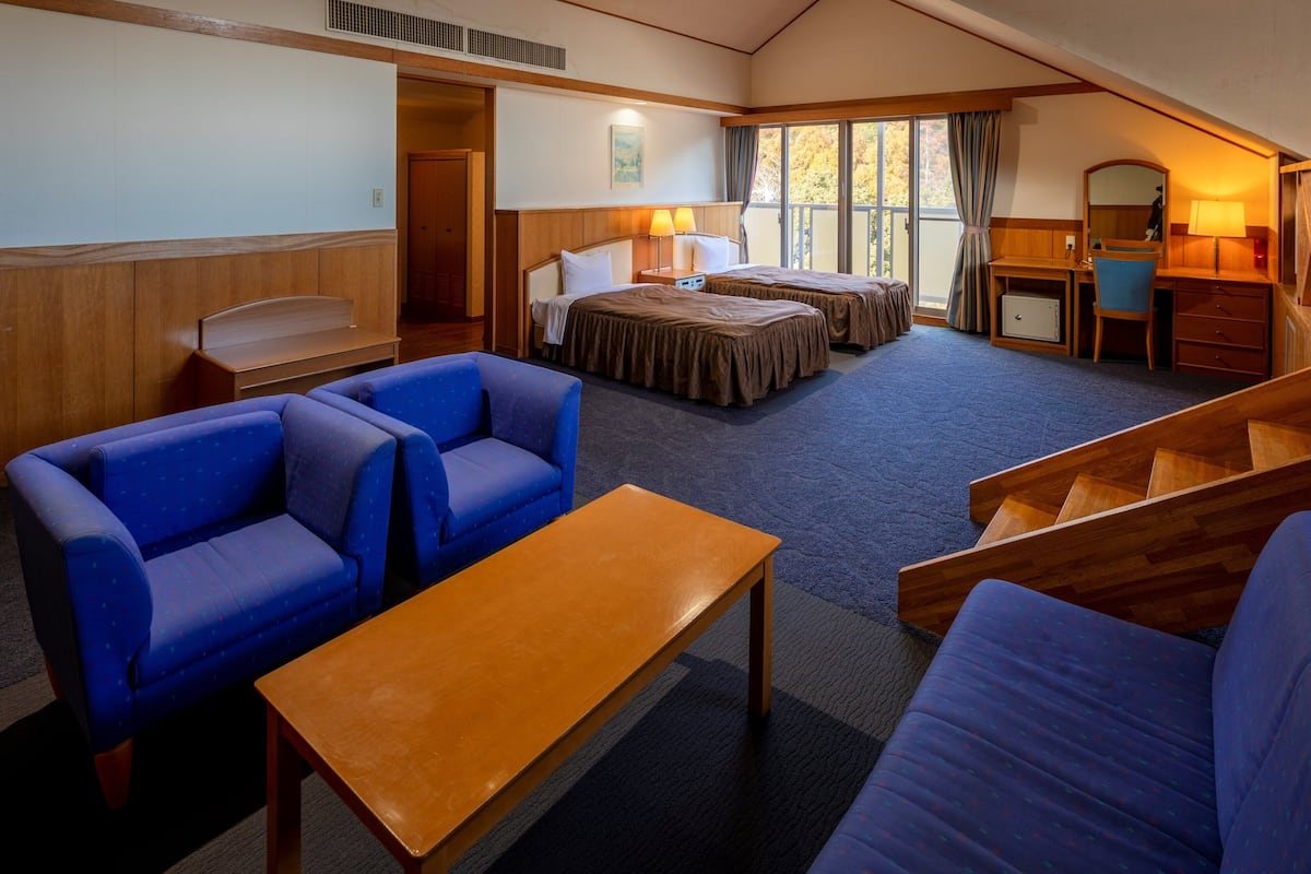 A hotel room with two beds, a desk, a chair, a sofa, and a small table.