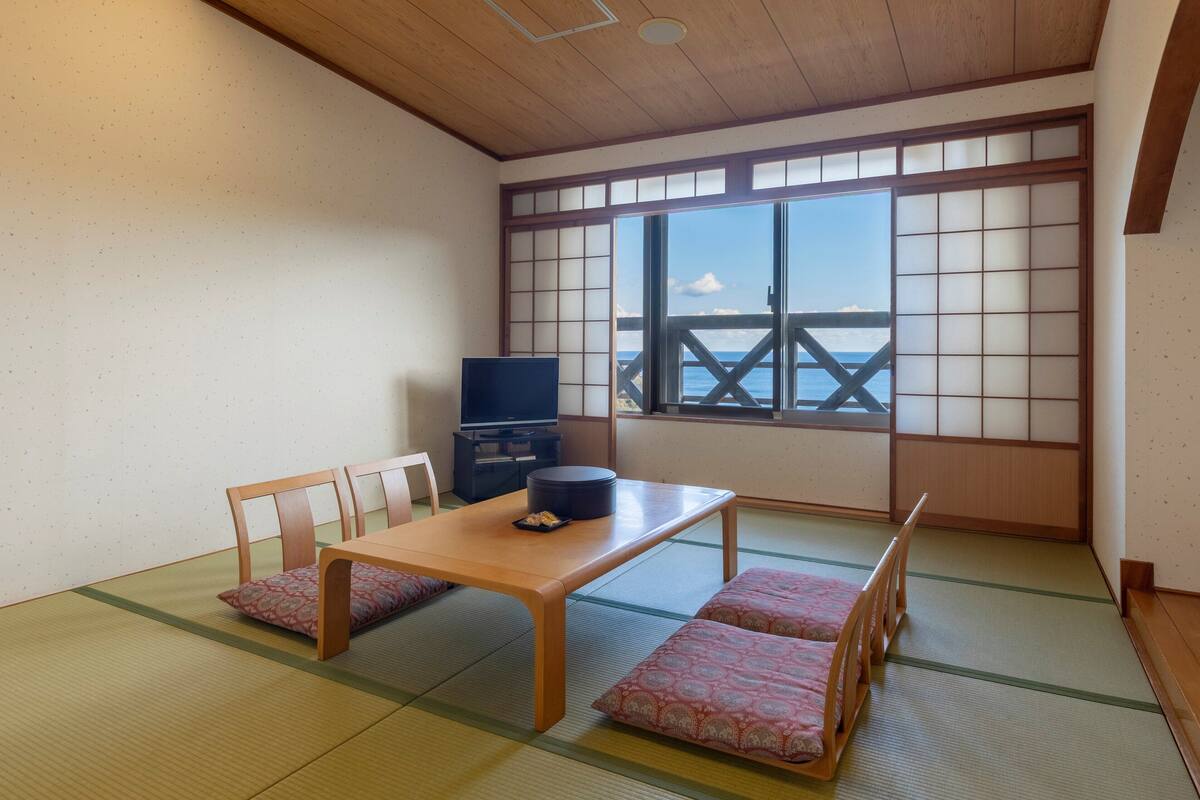 A traditional Japanese room with tatami flooring, a low wooden table, and a TV.