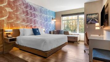 Une chambre d’hôtel moderne, dotée d’un grand lit, d’un bureau, d’une chaise et offrant une vue sur l’extérieur.