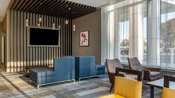 A modern lobby with a large flat-screen TV, seating areas with blue and brown chairs, and a patterned carpet.