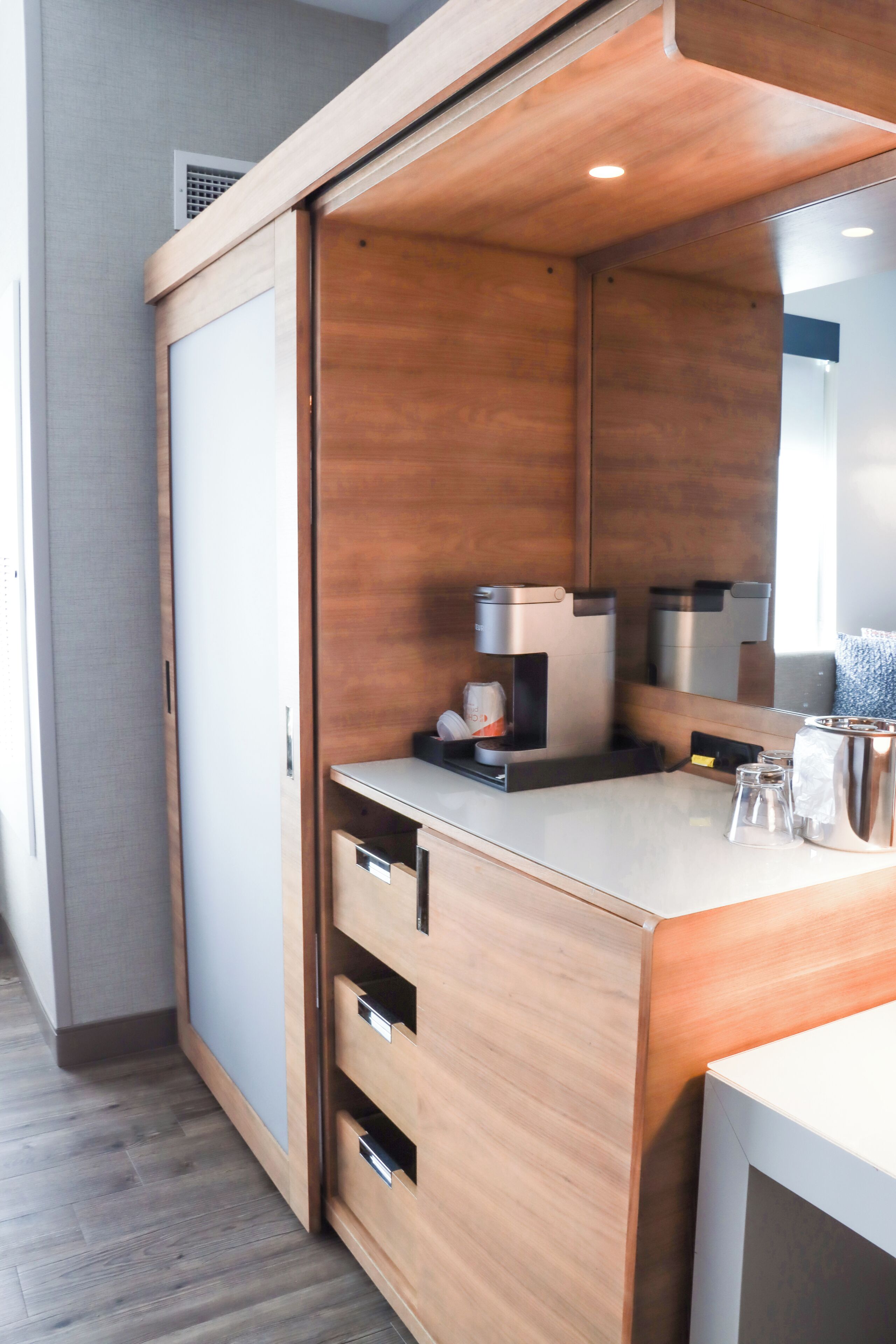 A modern bathroom with a wooden vanity, a mirror, and a coffee machine.