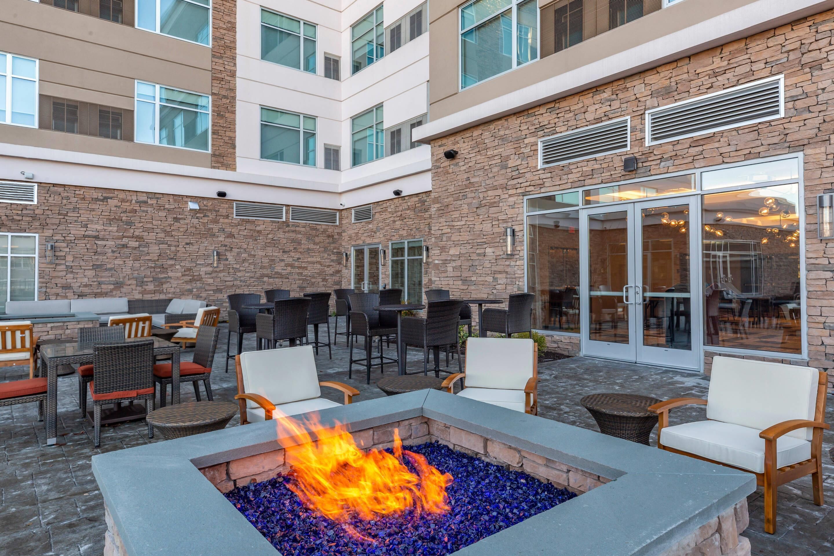 A courtyard with outdoor seating, a fire pit, and a building with stone facade and large windows.