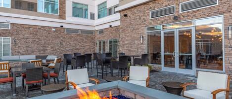 A courtyard with outdoor seating, a fire pit, and a building with stone facade and large windows.