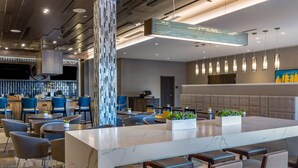 Un moderno vestíbulo de hotel con un mostrador de recepción de mármol, asientos de bar y una amplia zona de estar con sofás y sillones.