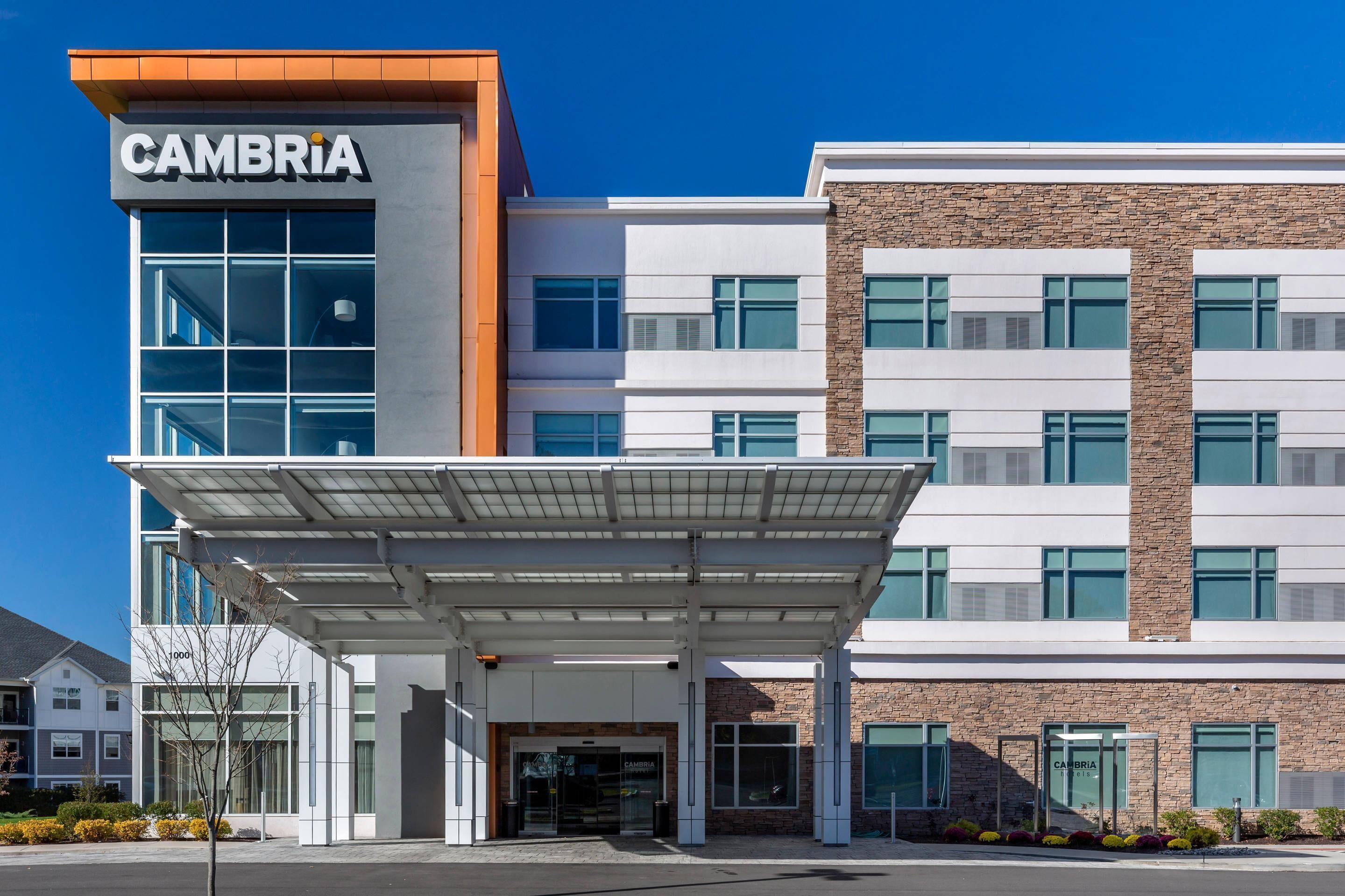 A modern building with a 'CAMBRIA' sign, a covered entrance, and a clear blue sky.