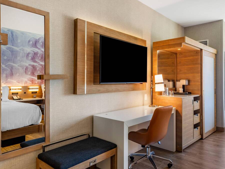 A hotel room with a bed, a desk, a chair, a television, and a mirror.