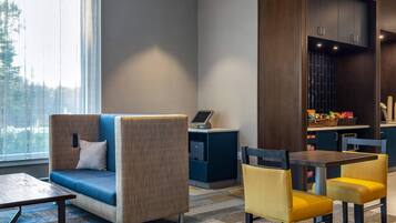 A modern hotel lobby with a sofa, chairs, a desk with a computer, and a view of the outdoors.